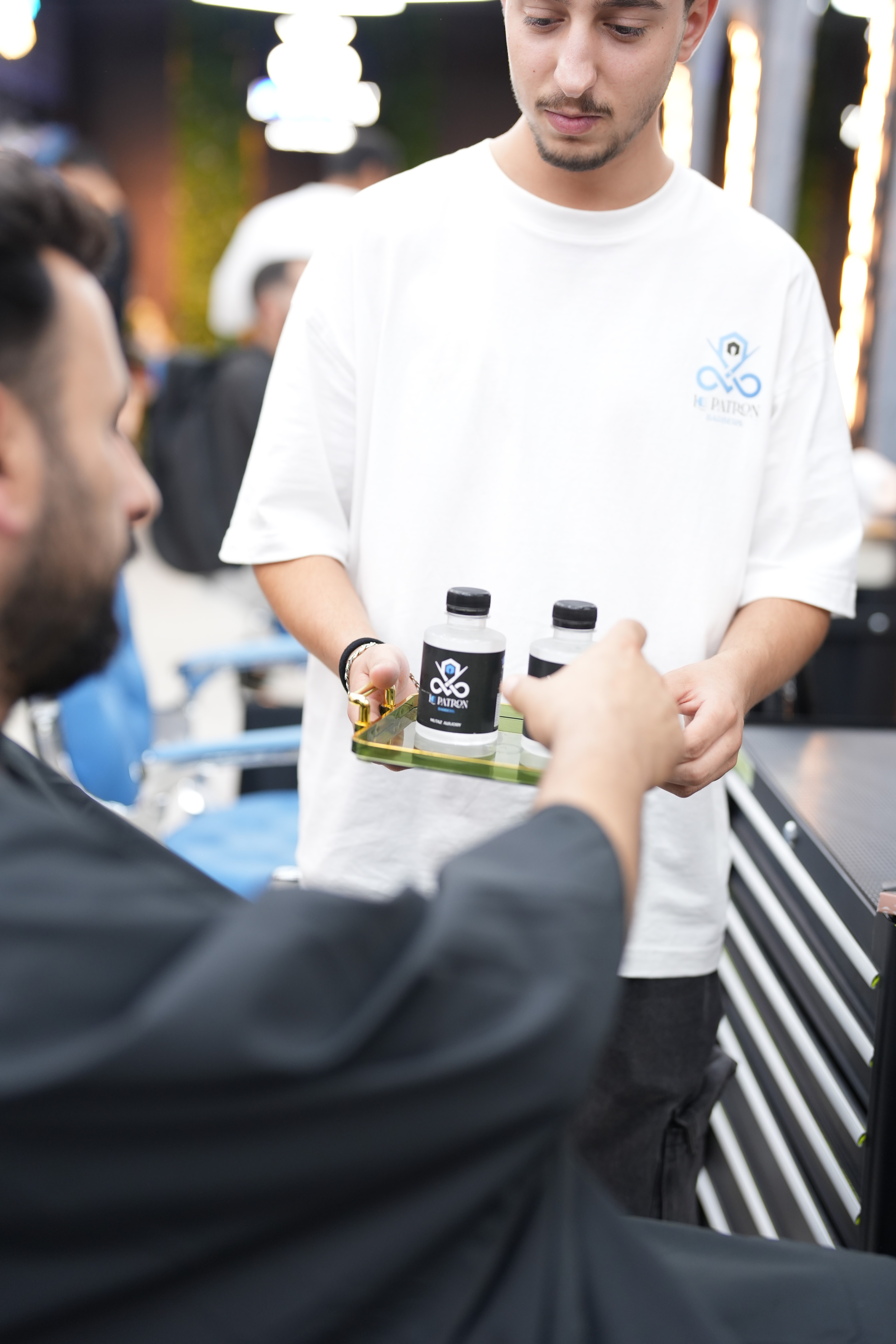 A Le Patron staff member serving bottled water on a tray to a seated client