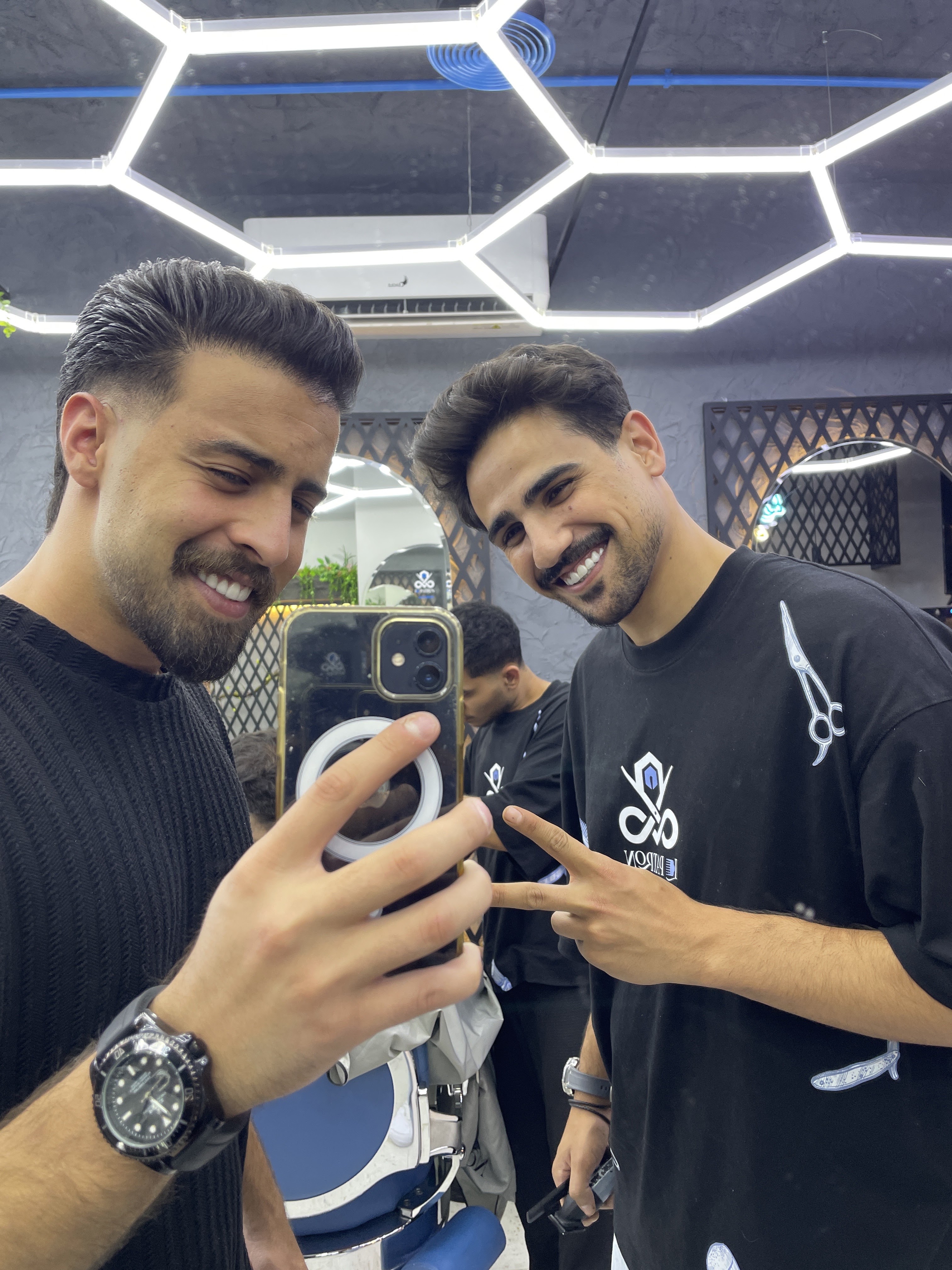 Two clients smiling and showing off their fresh haircuts inside the shop