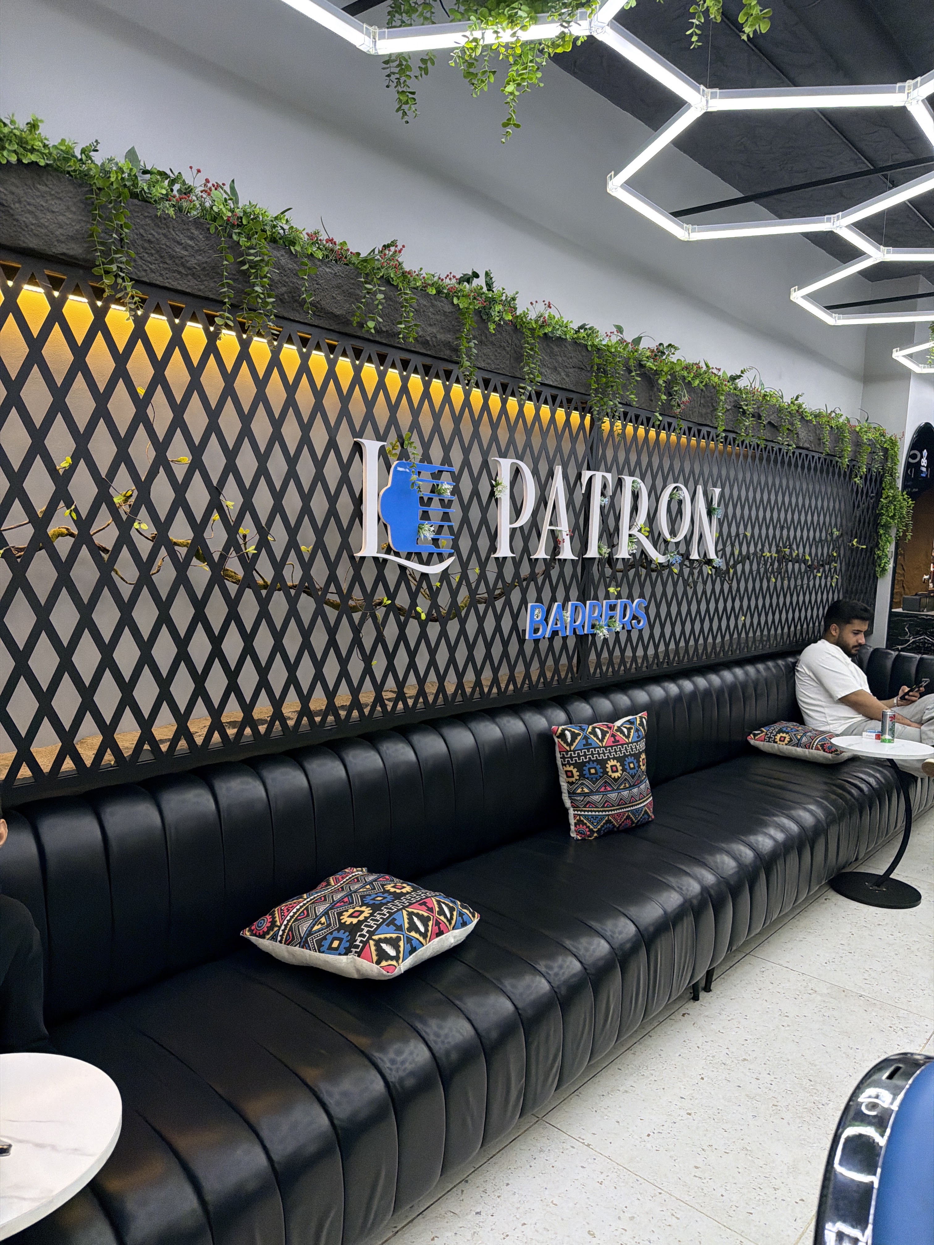 The Le Patron Barbers wall sign above a long black leather lounge with embroidered cushions