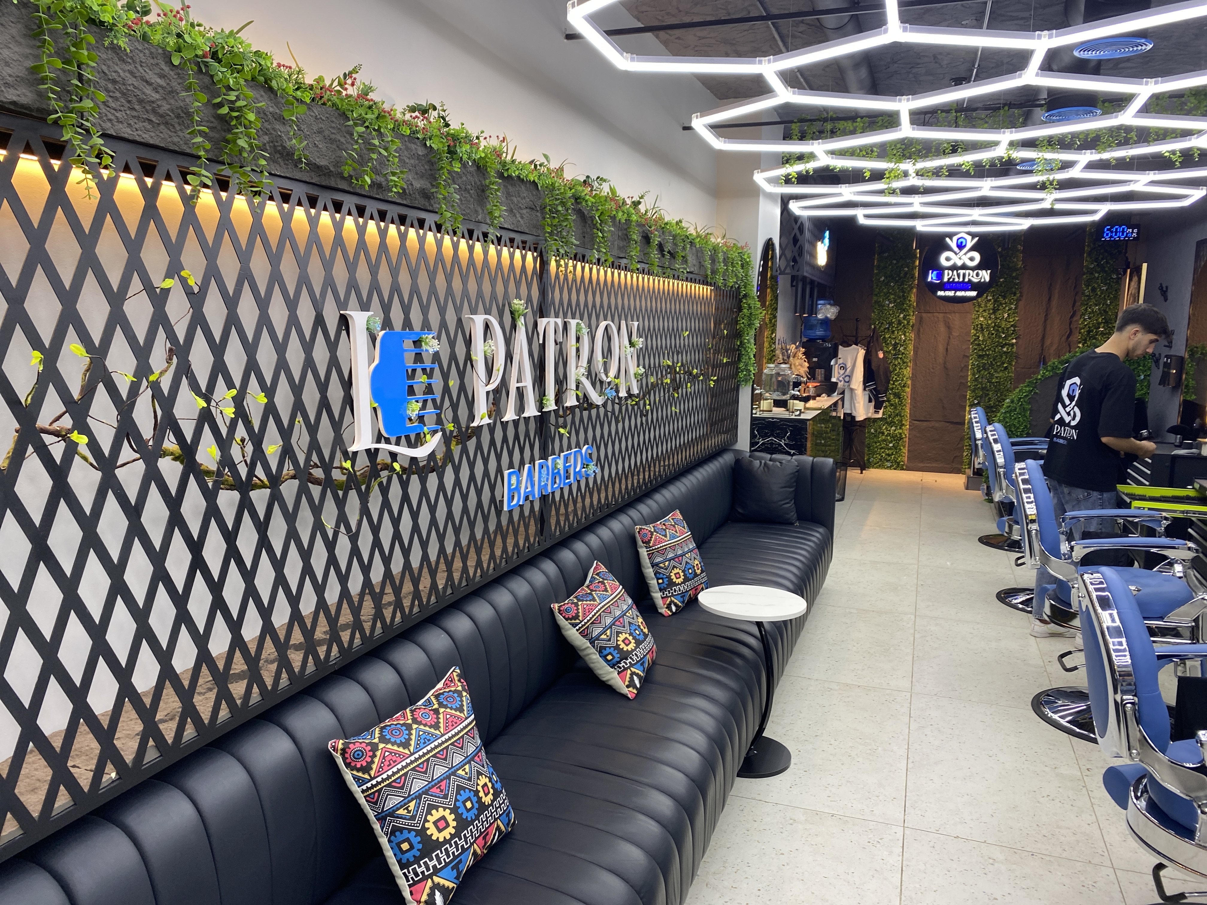 Le Patron Barbers lounge leading back to the row of barber chairs, plants and signage lit warmly